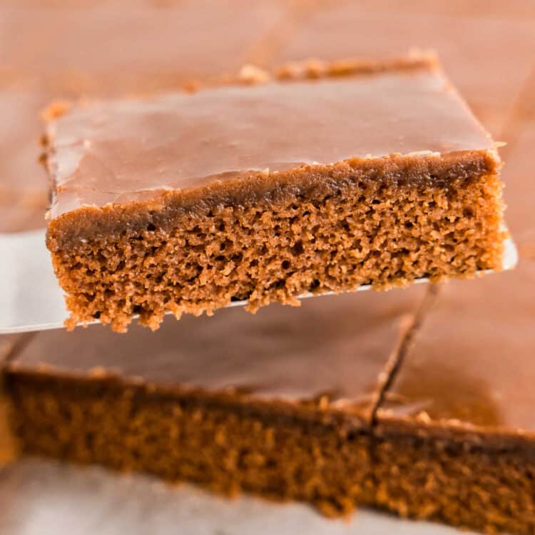 Texas Sheet Cake cut into squares and using spatula to remove a piece from pan