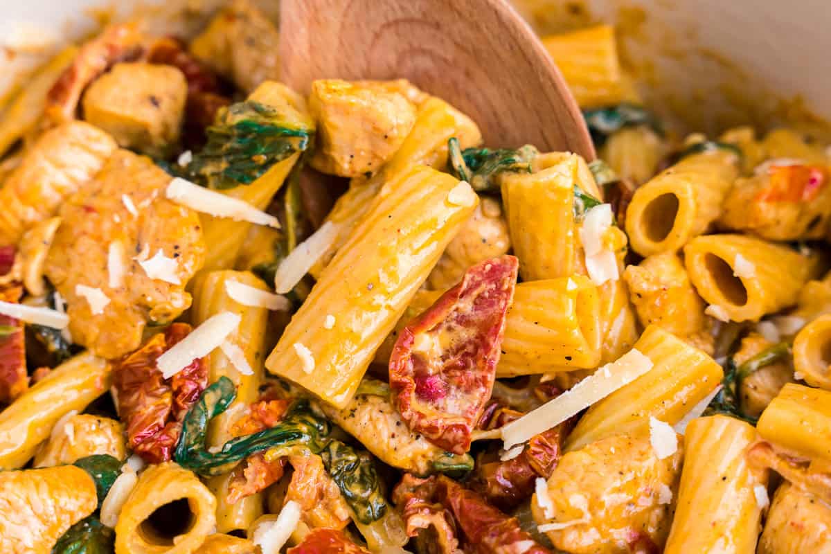 Creamy Tuscan Chicken Pasta being stirred with wooden spoon