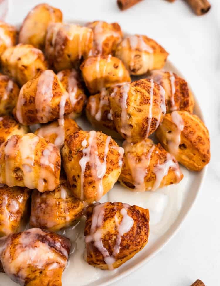 White Plate with Cinnamon Roll Bites on top and cinnamon sticks laying around the plate.