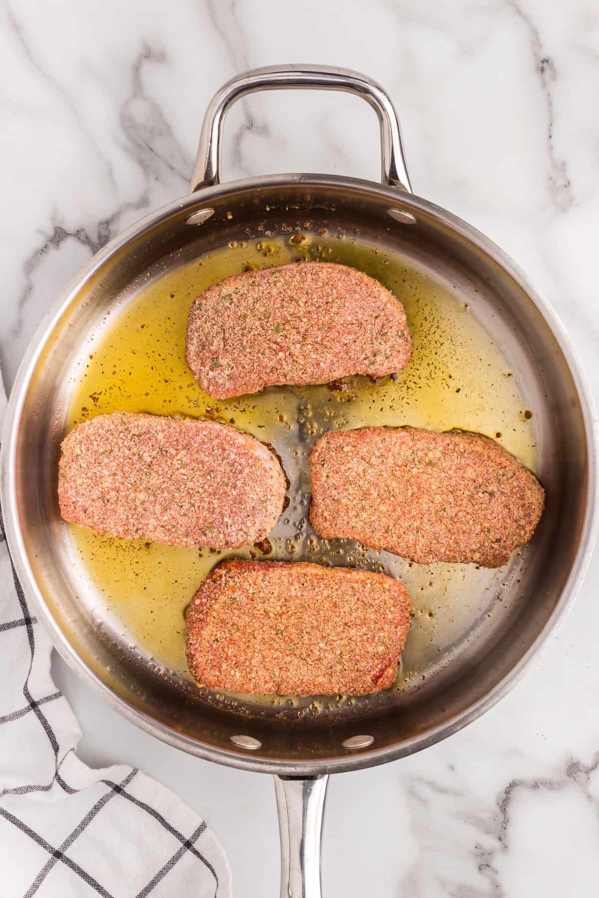 Coated pork chops in skillet with olive oil for Parmesan Crusted Pork Chops recipe