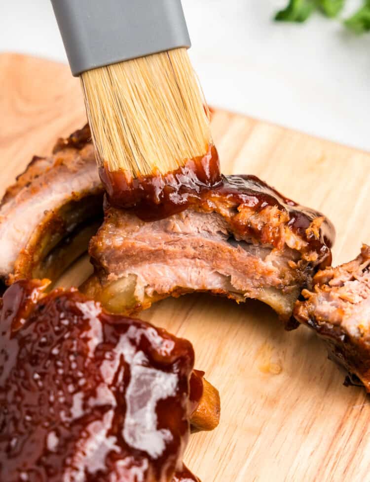 Brushing BBQ sauce on Oven Baked Pork Ribs on wooden cutting board