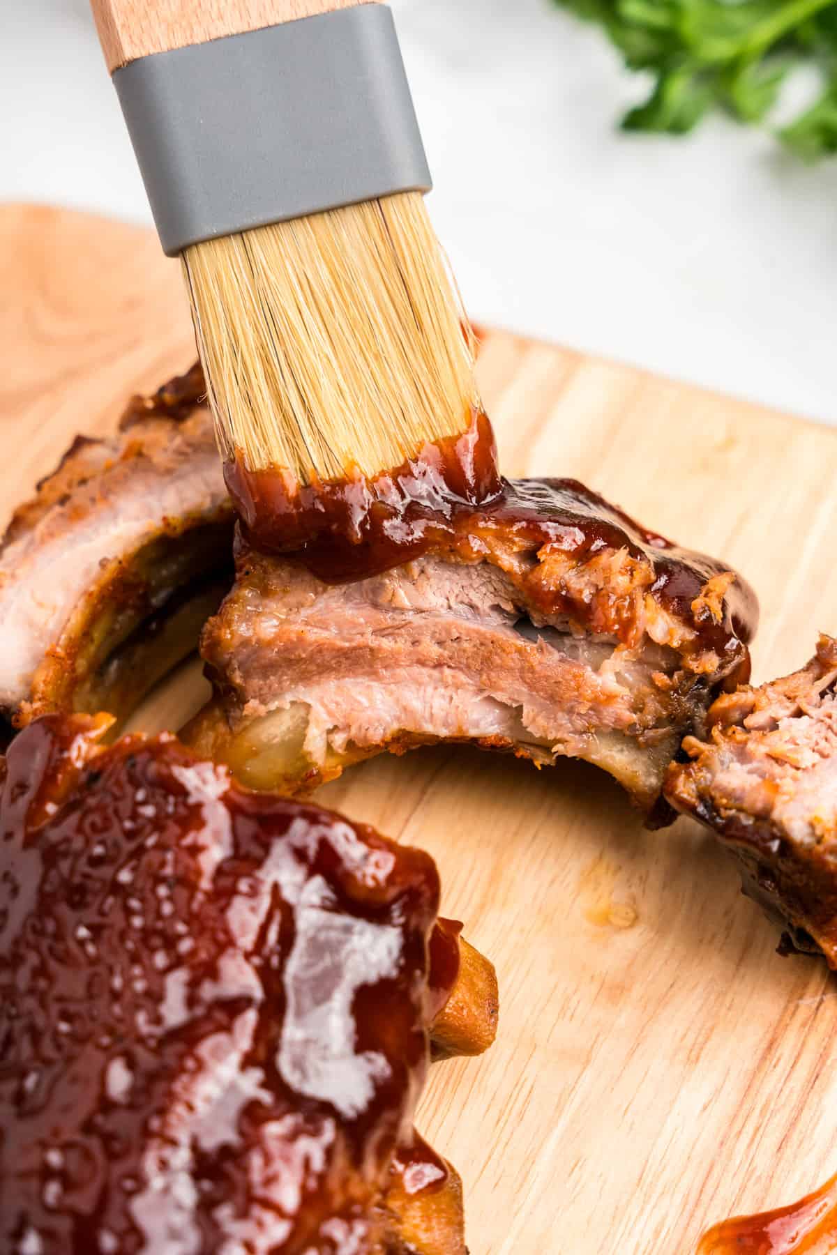 Brushing BBQ sauce on Oven Baked Pork Ribs on wooden cutting board