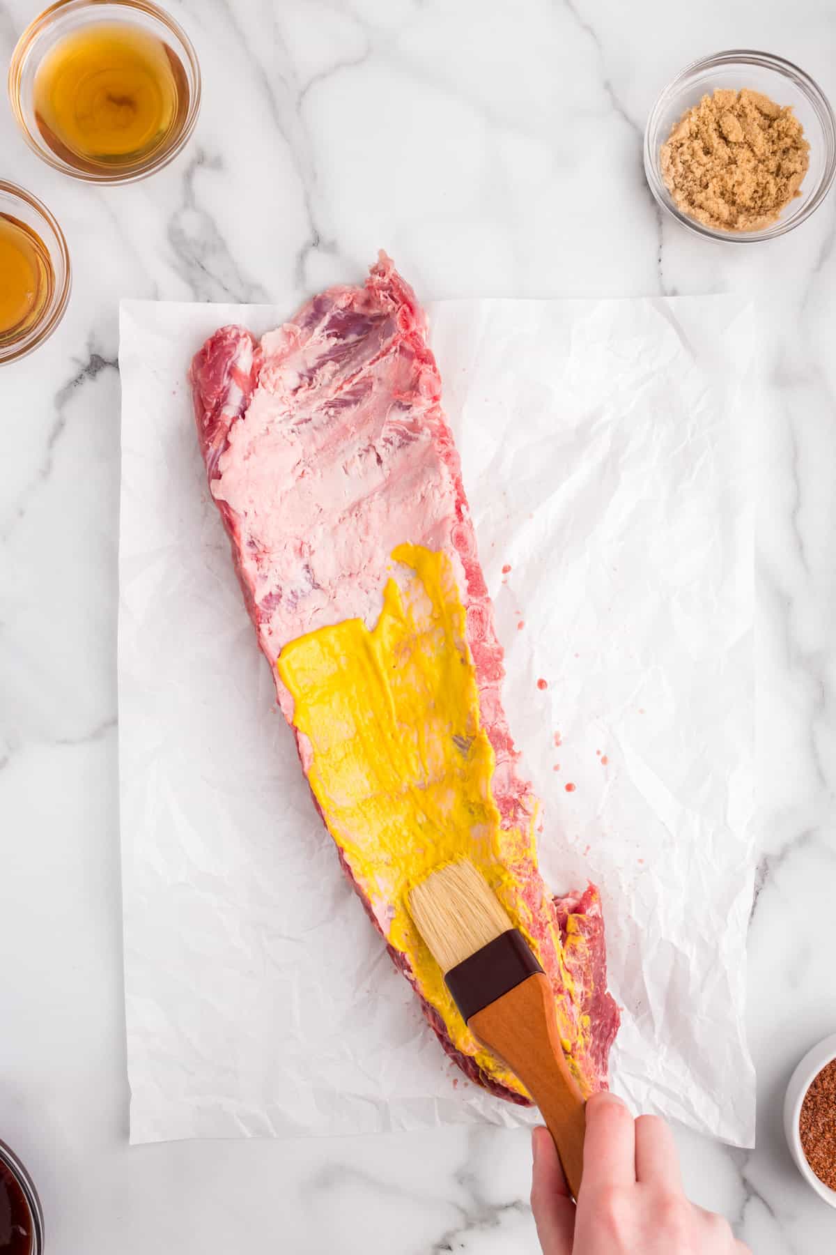 Brushing mustard on baby back ribs over parchment paper for Oven Baked Ribs recipe