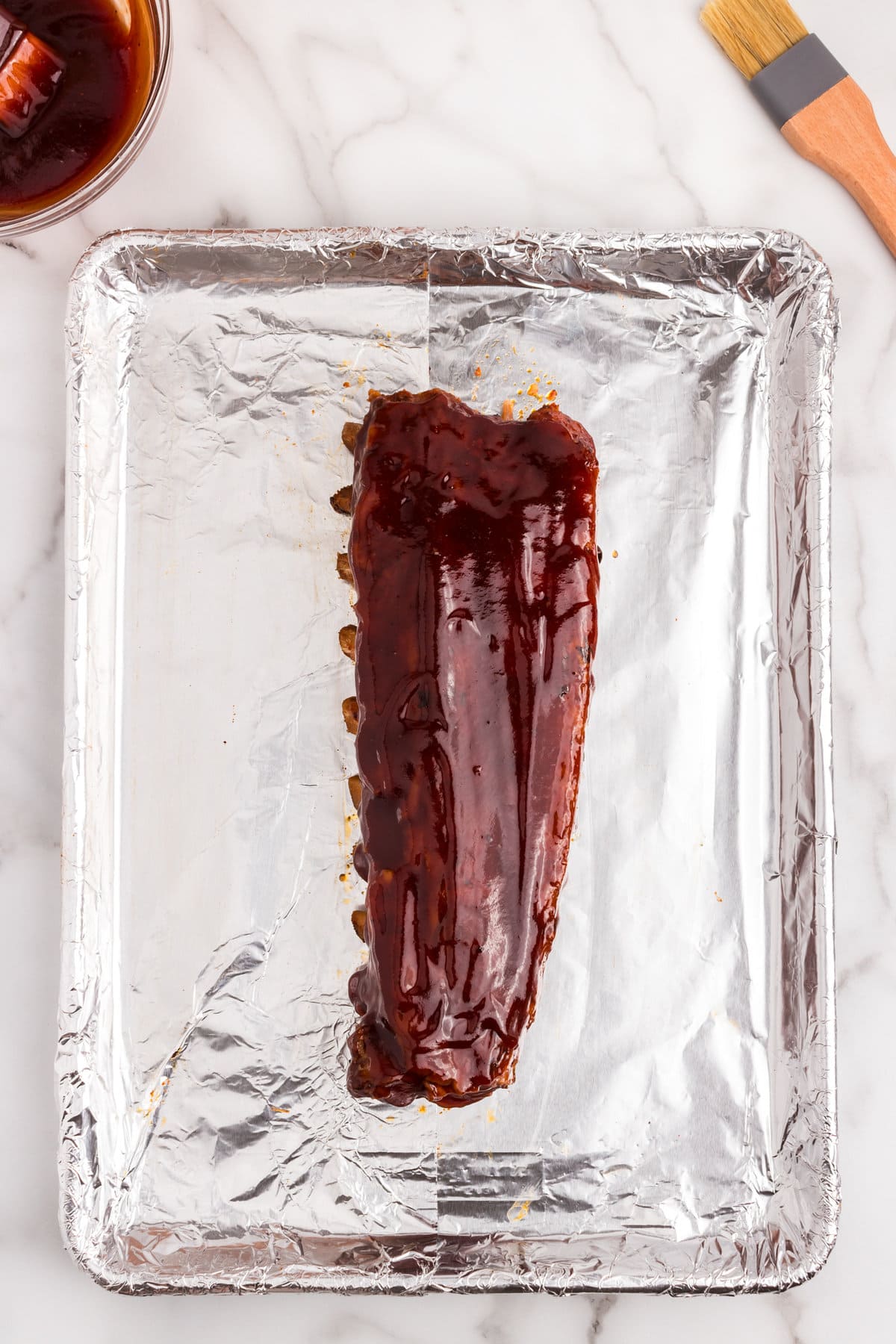 Oven Baked Ribs brushed with BBQ sauce on tinfoil-lined baking sheet