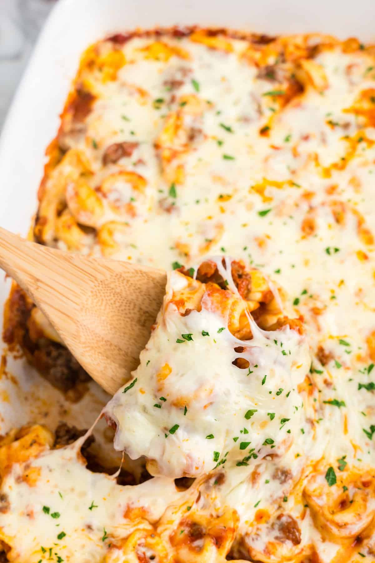 Using wooden spoon to scoop the first bite of Baked Tortellini 