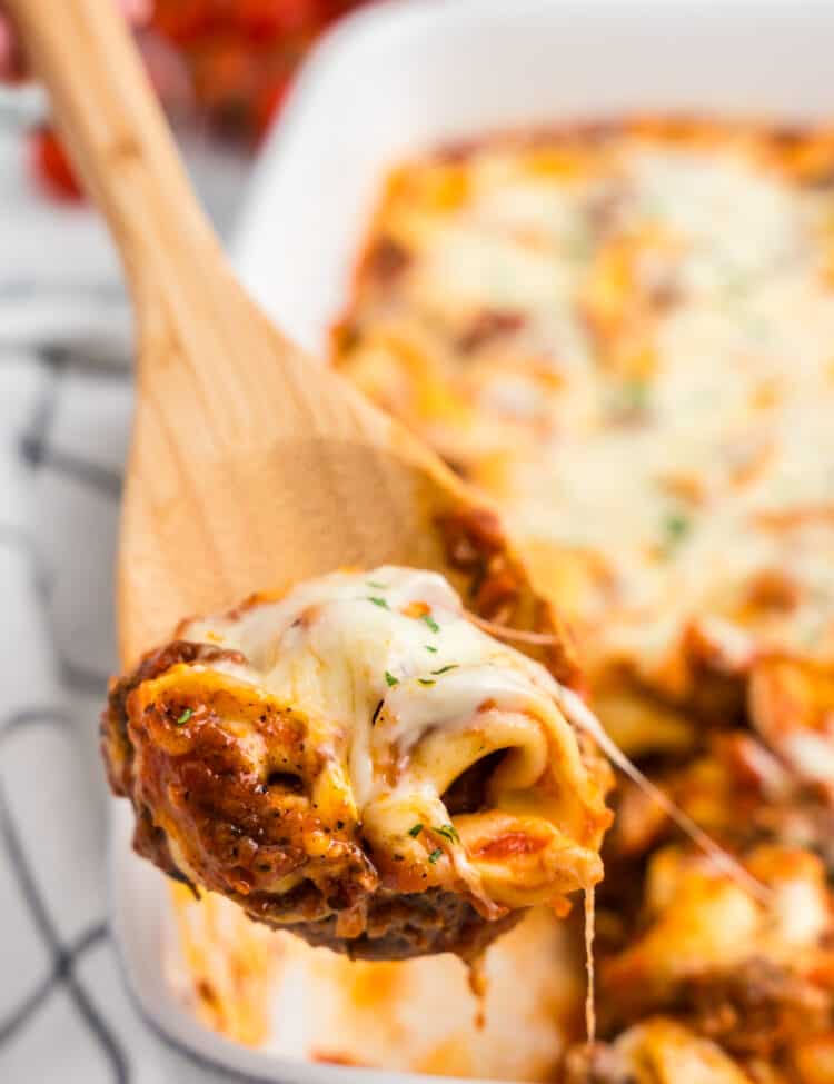 Using wooden spoon to scoop Baked Tortellini from baking dish