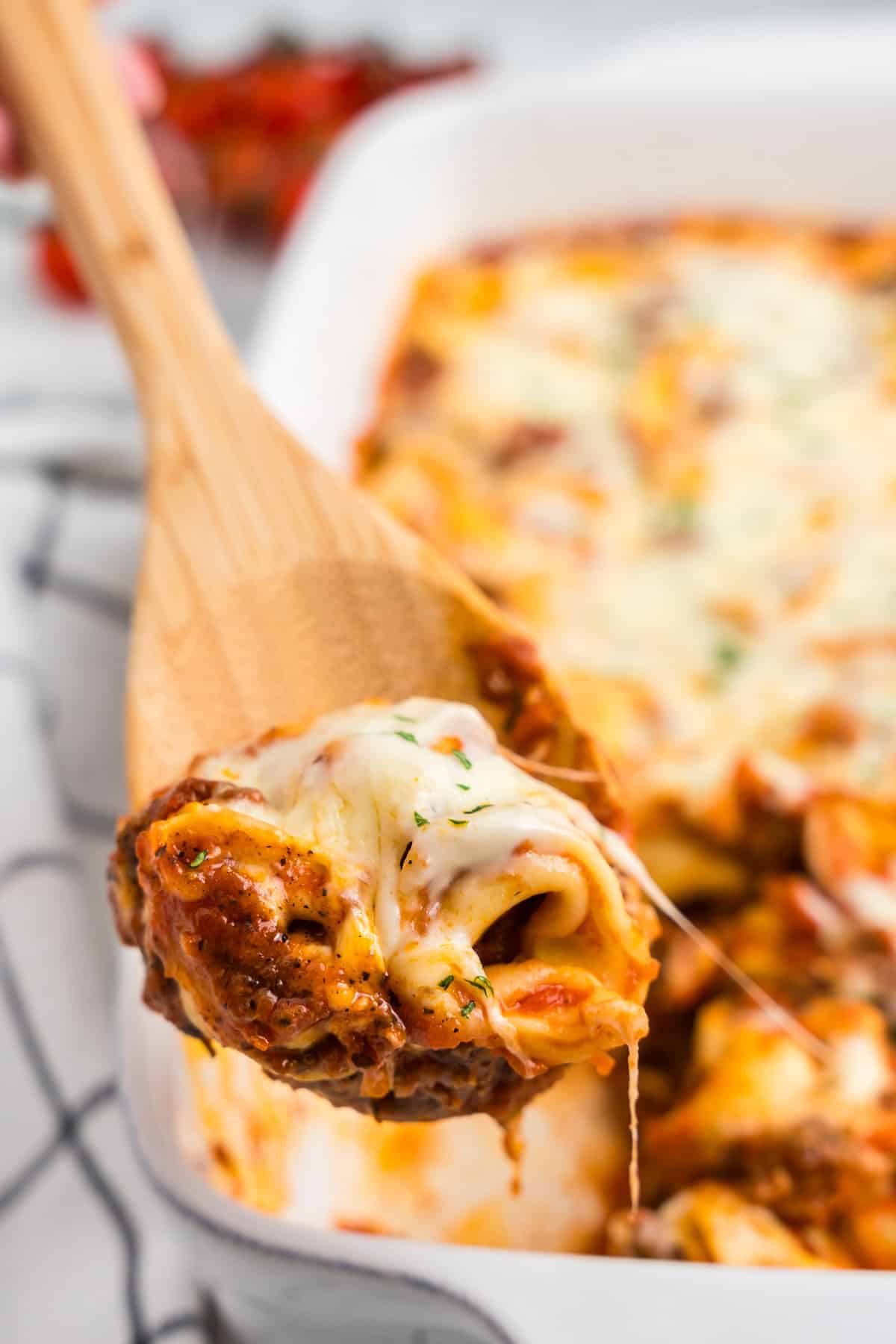 Using wooden spoon to scoop Baked Tortellini from baking dish