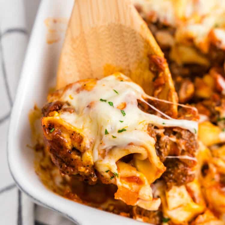 Closeup square image of Baked Tortellini being scooped from the baking pan