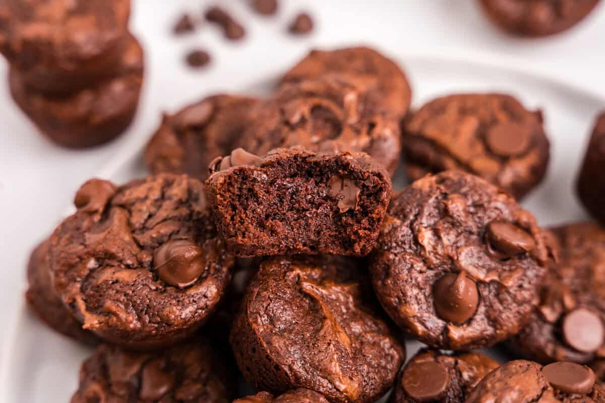 a pile of brownie bites piled up on a plate with a bite taken out of the top one.