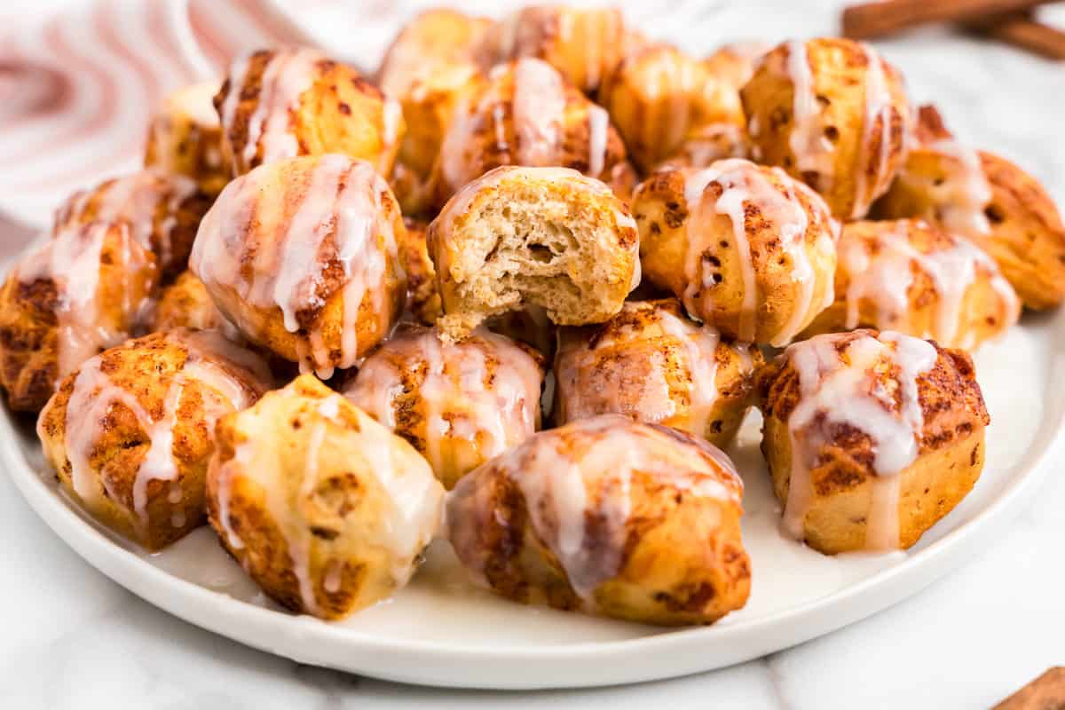 A White plate full of cinnamon roll bites with one having a bite taken out of it.