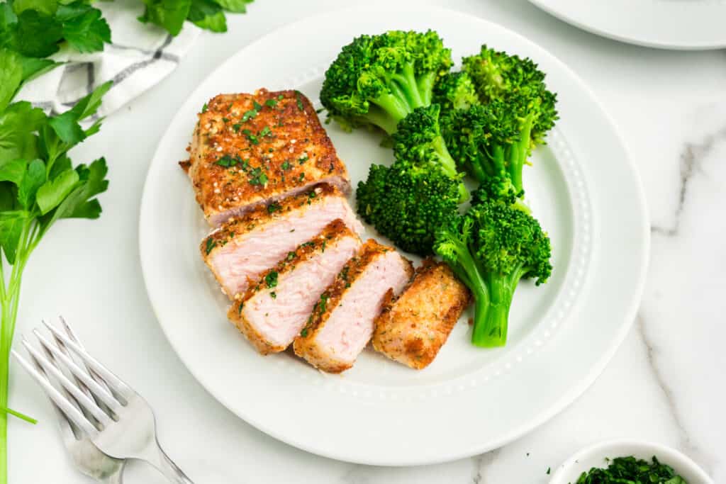 Baked Pork chops with parmesan crusting on white plate with broccoli