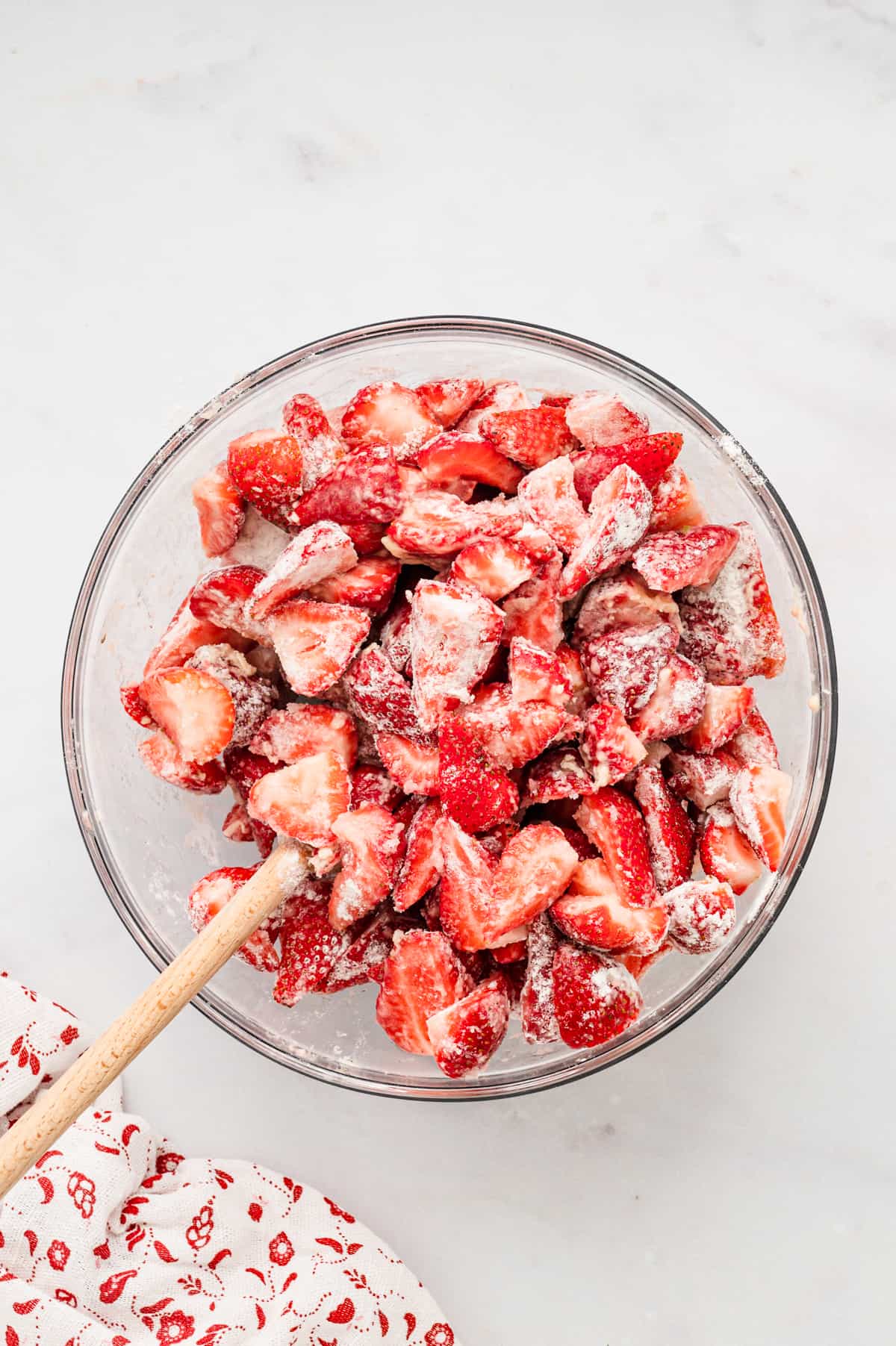 Mixing together strawberries and filling ingredients in glas mixing bowl with wooden spoon for Strawberry Crisp Recipe