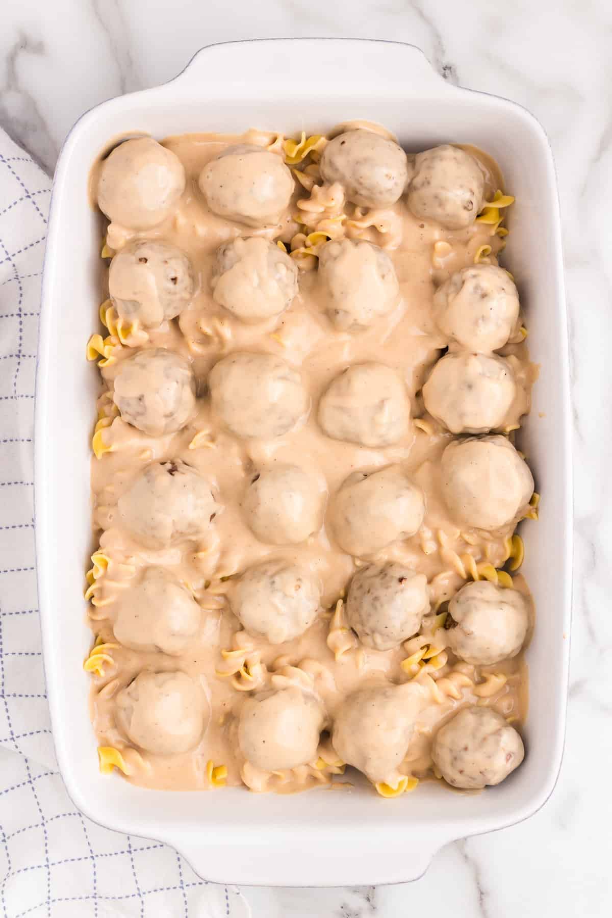 Meatballs and gravy over egg noodles in 9x13 baking dish for Swedish Meatball Casserole