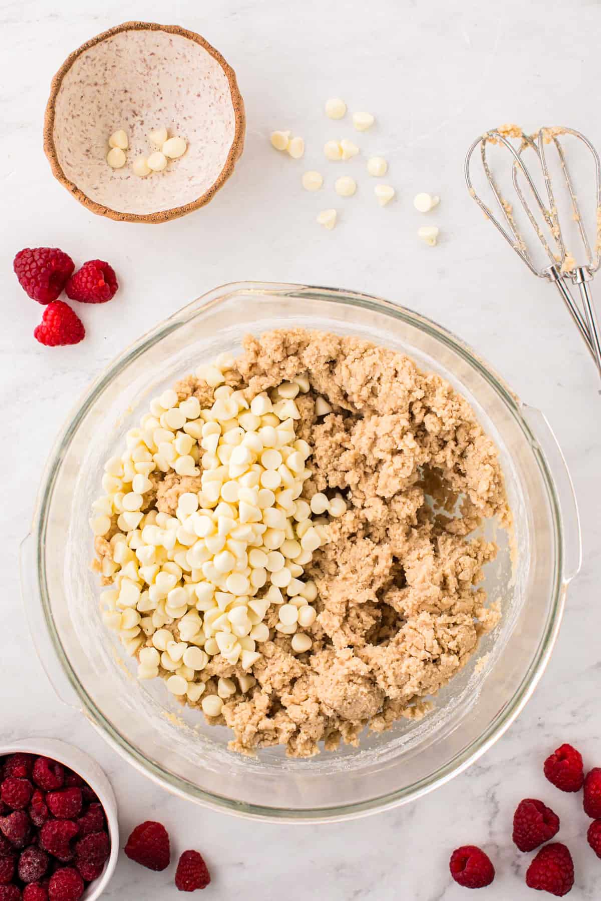 Adding white chocolate chips to cookie dough in mixing bowl for Raspberry & White Chocolate Cookies