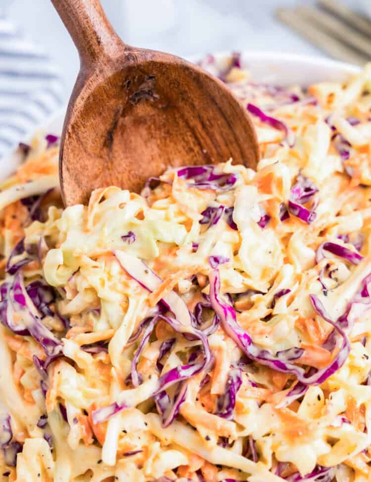 Using wooden spoon to scoop Creamy Coleslaw from serving bowl