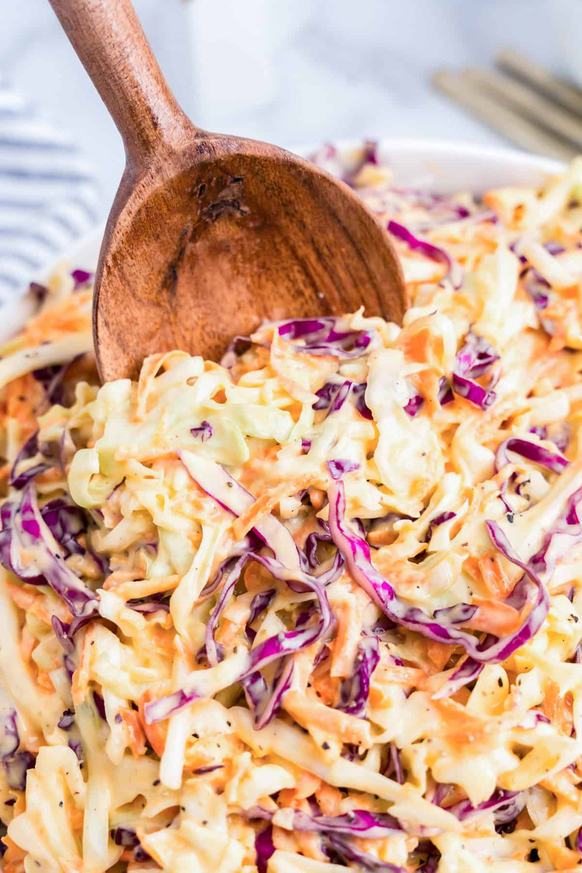 Using wooden spoon to scoop Creamy Coleslaw from serving bowl