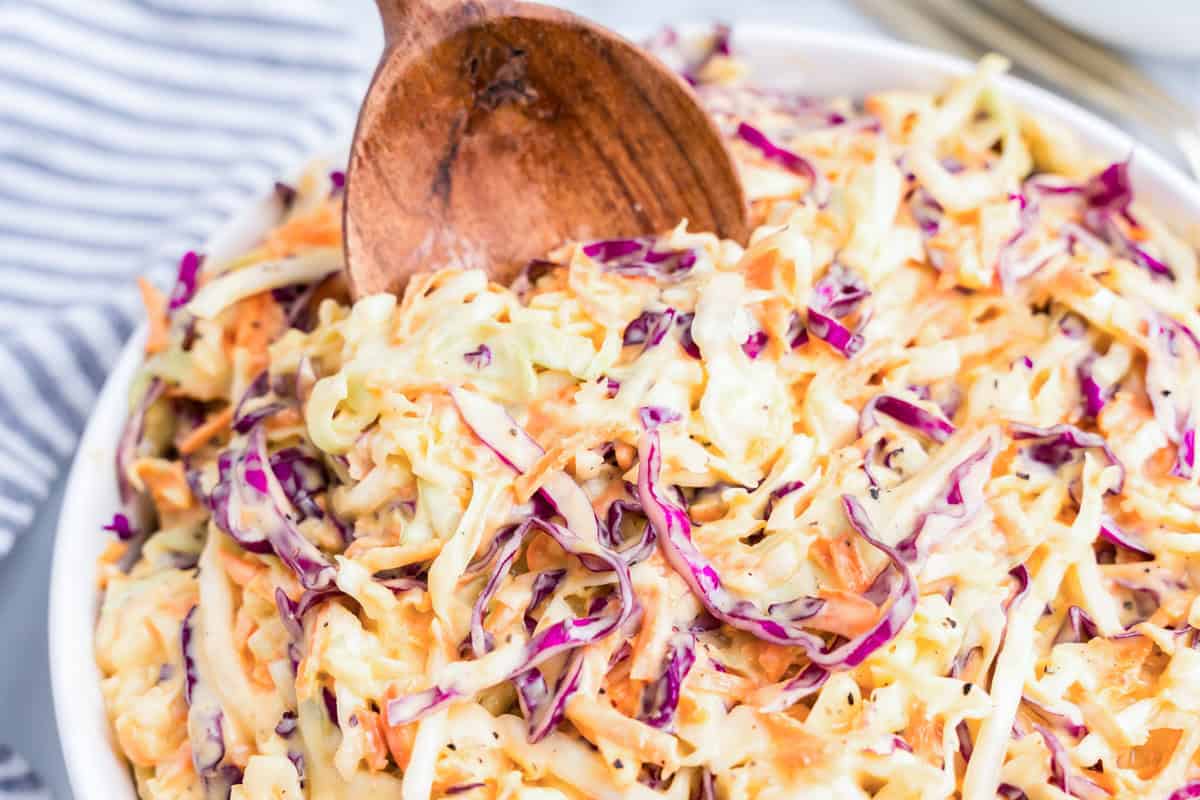 Using wooden spoon to scoop Creamy Coleslaw from serving bowl