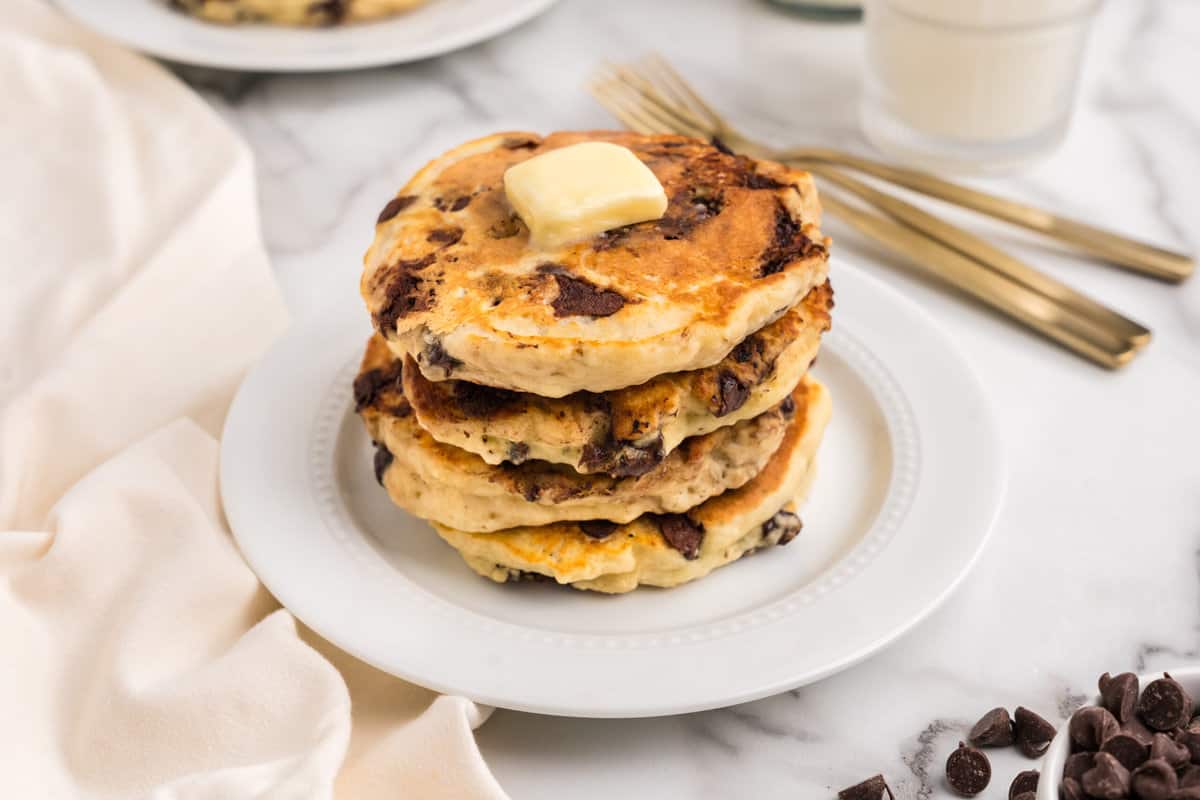 Stack of pancakes on a white plate waiting for syrup.