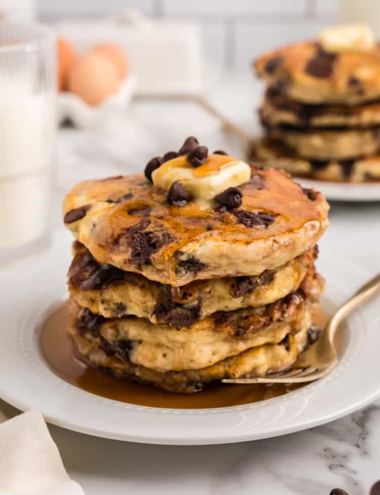 Stack of pancakes displayed on a white plate with a piece of butter on top.