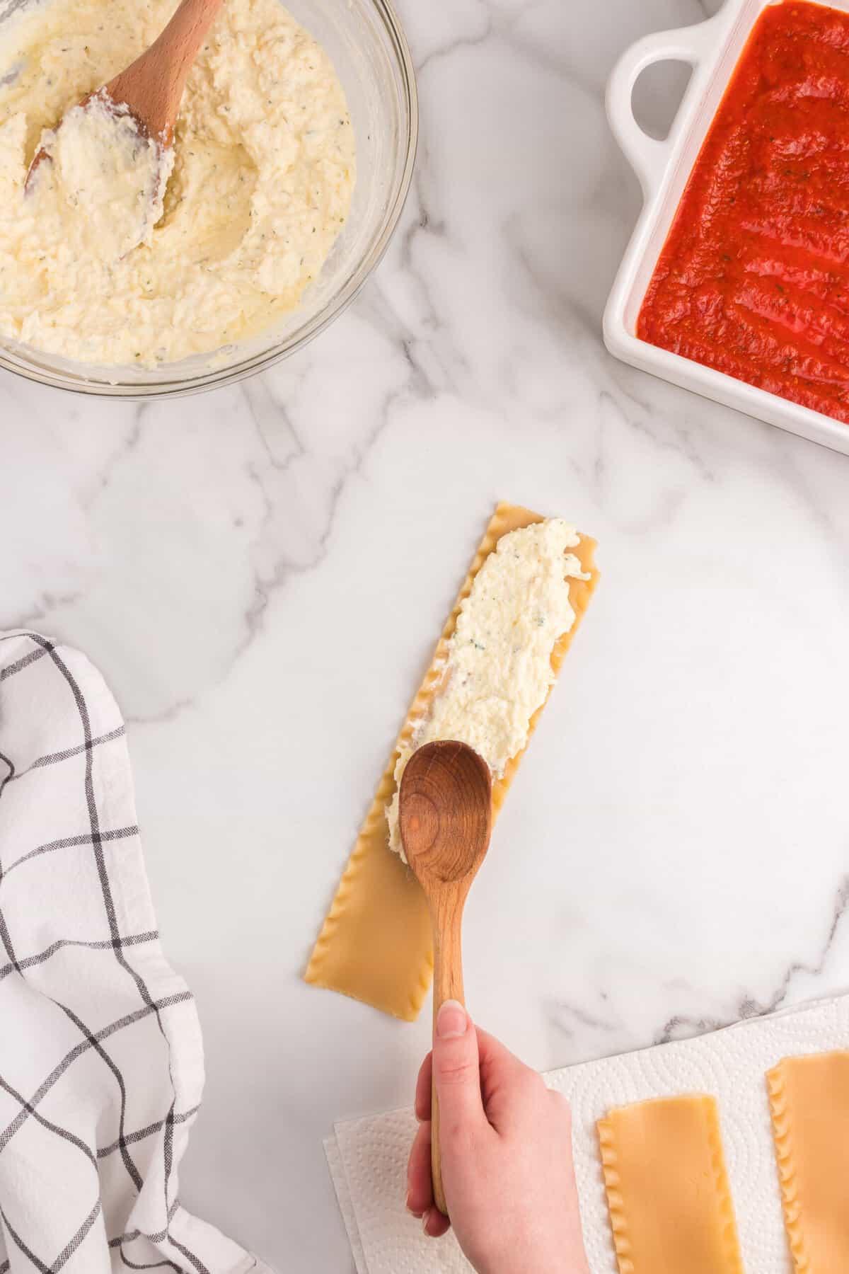 Spooning and spreading the cheese mixture on cooked lasagna noodle for Lasagna Roll Ups recipe