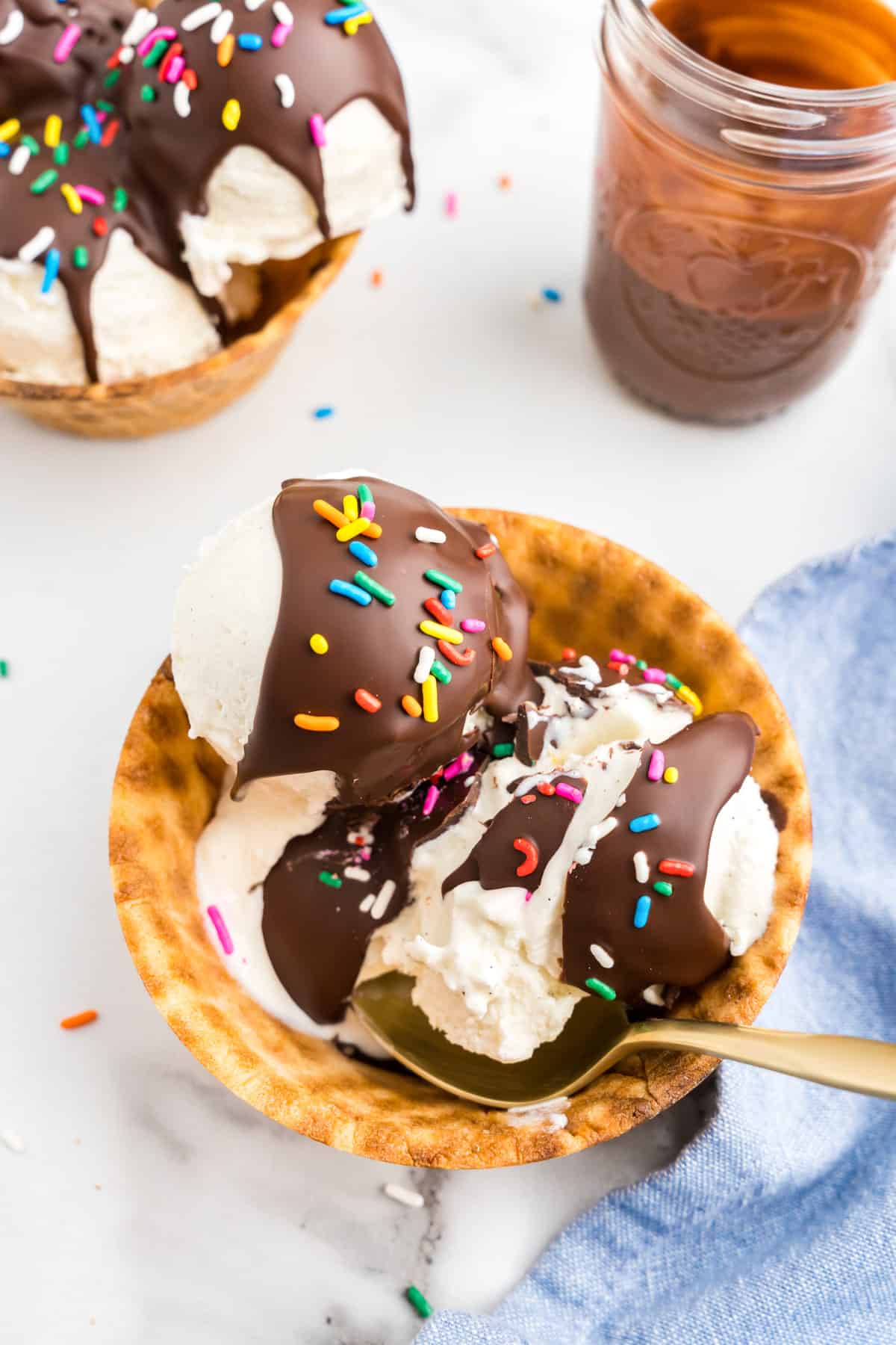 Homemade Magic Shell topped with sprinkles over vanilla ice cream in waffle cone sundae bowl