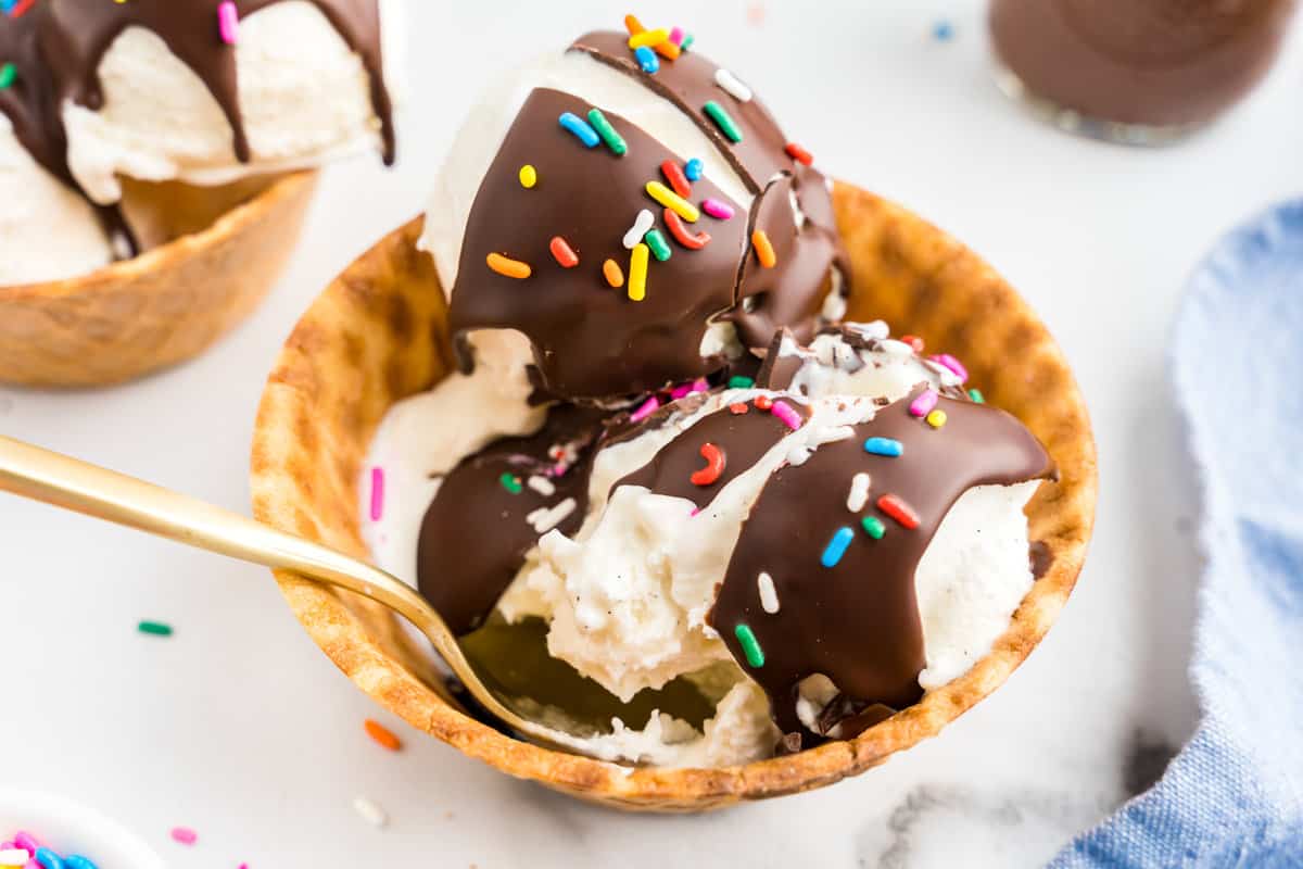 Homemade Magic Shell topped with sprinkles over vanilla ice cream in waffle cone sundae bowl