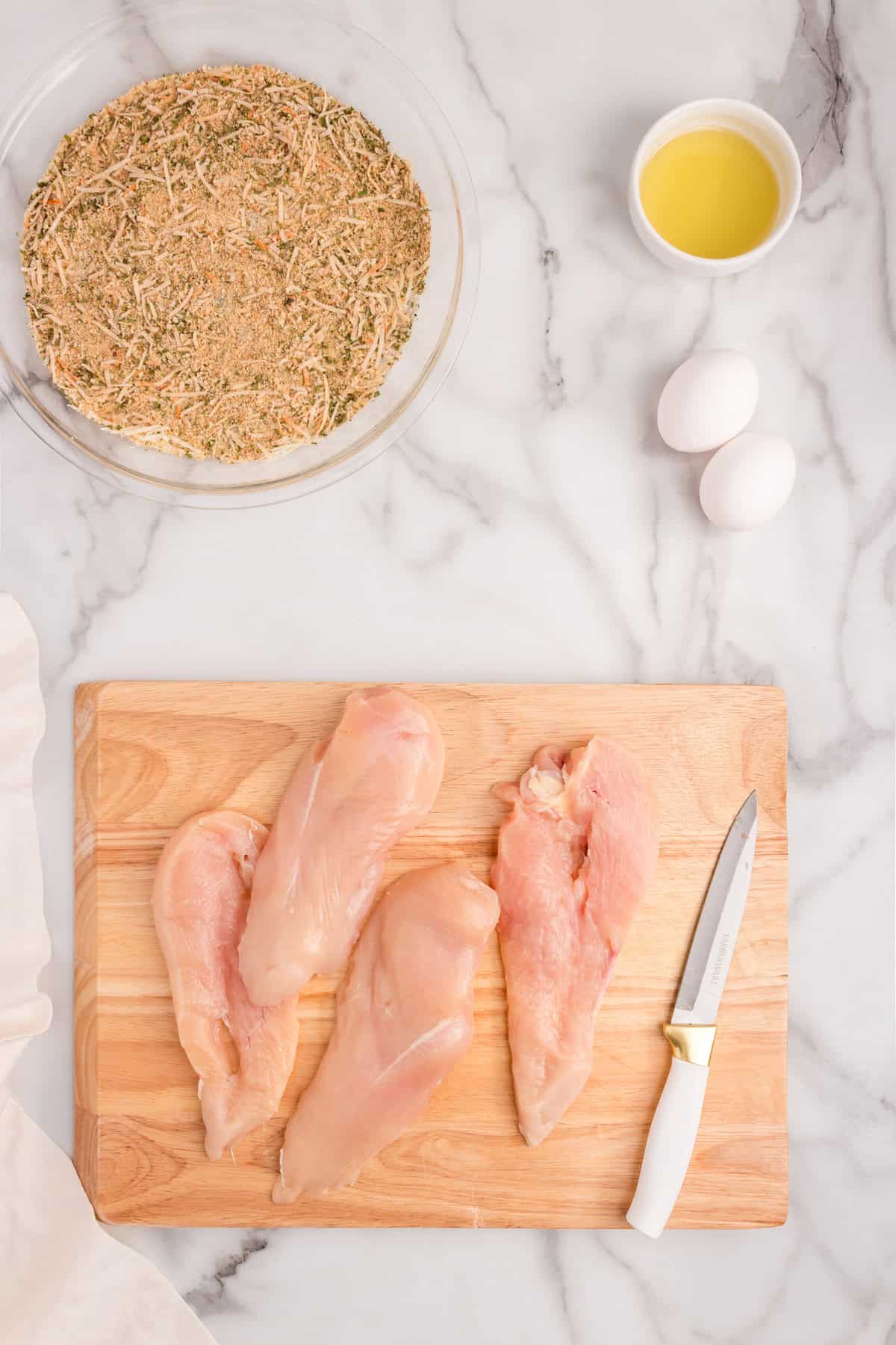 Prepared chicken breasts on wooden cutting board for Parmesan Crusted Chicken recipe
