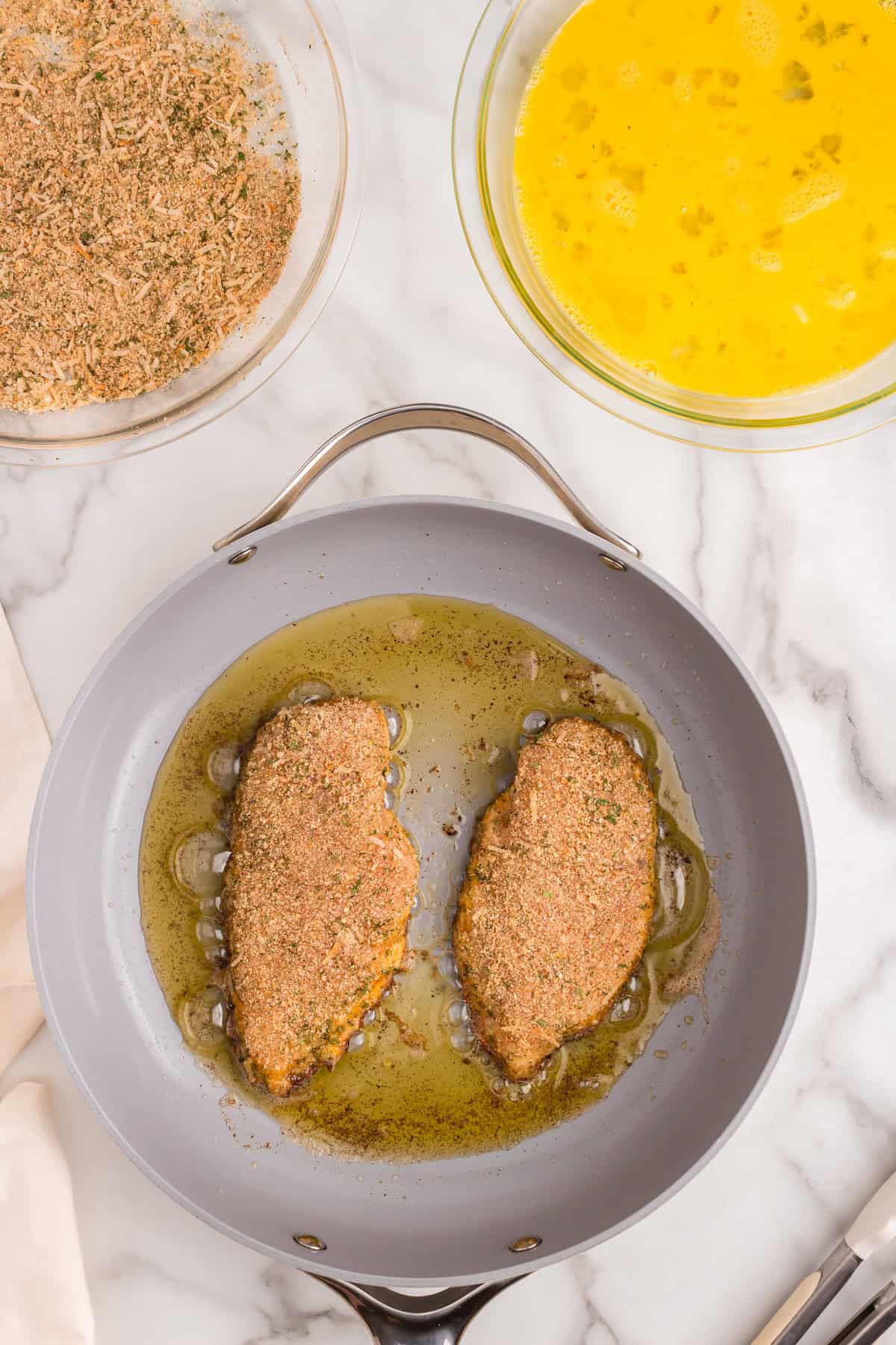 Frying coated and seasoned chicken breast in stovetop skillets for Parmesan Crusted Chicken