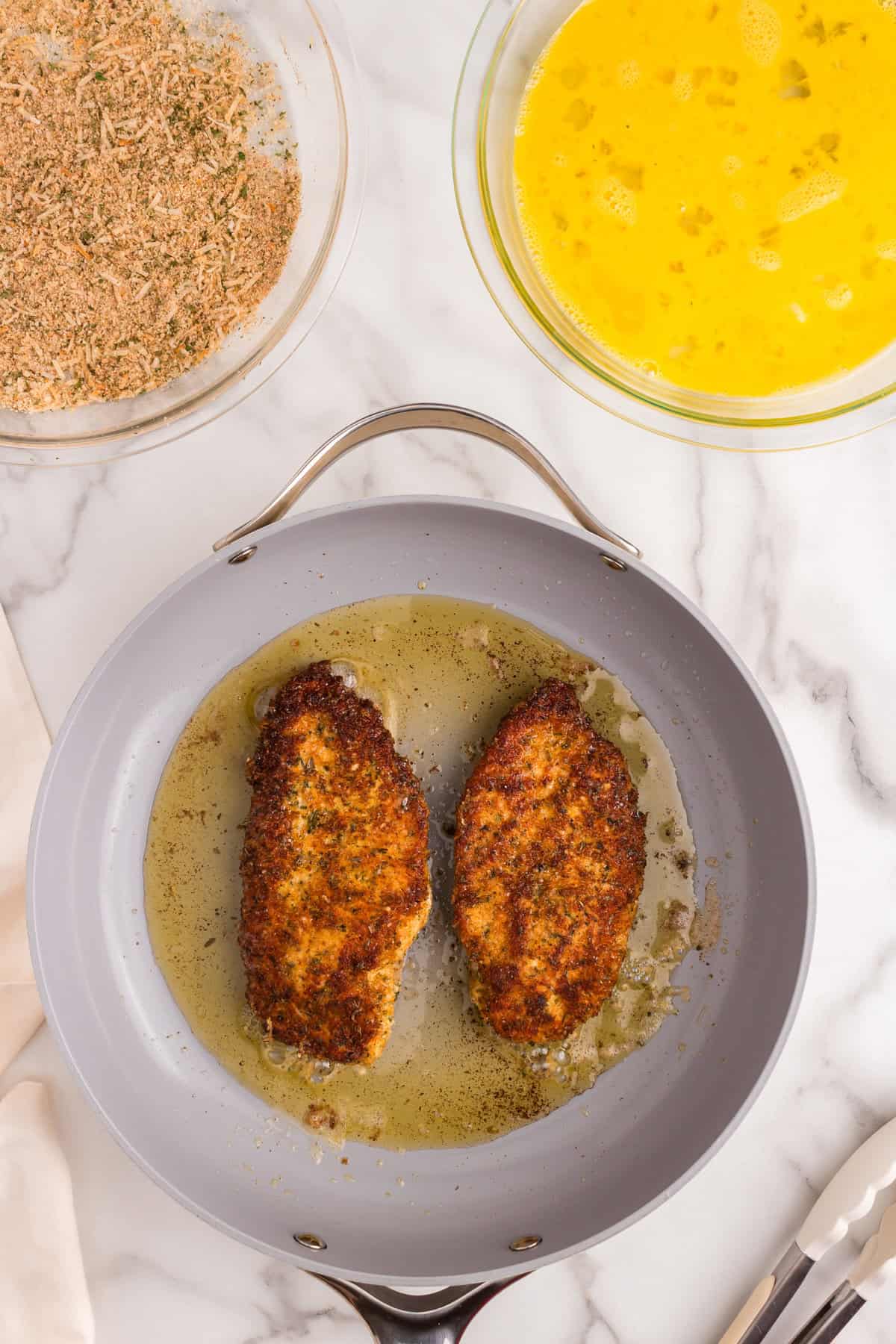 Perfectly browned and crusted Parmesan Crusted Chicken breasts in stovetop skillet