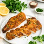 White plate with Parmesan Crusted Chicken on it, one sliced