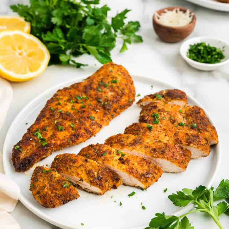White plate with Parmesan Crusted Chicken on it, one sliced