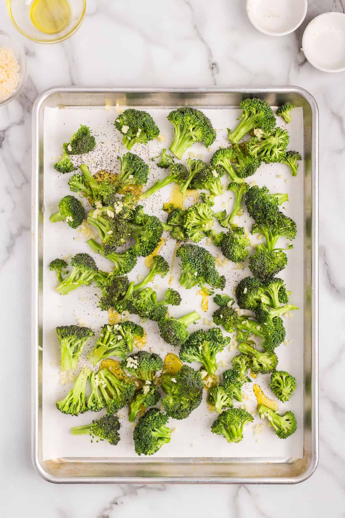 Adding seasonings to broccoli on parchment-lined cooking sheet for Roasted Broccoli recipe