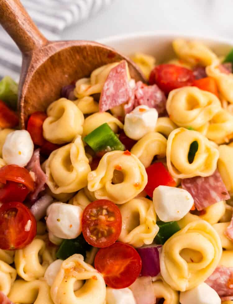 Using wooden spoon to scoop Tortellini Pasta Salad from serving bowl