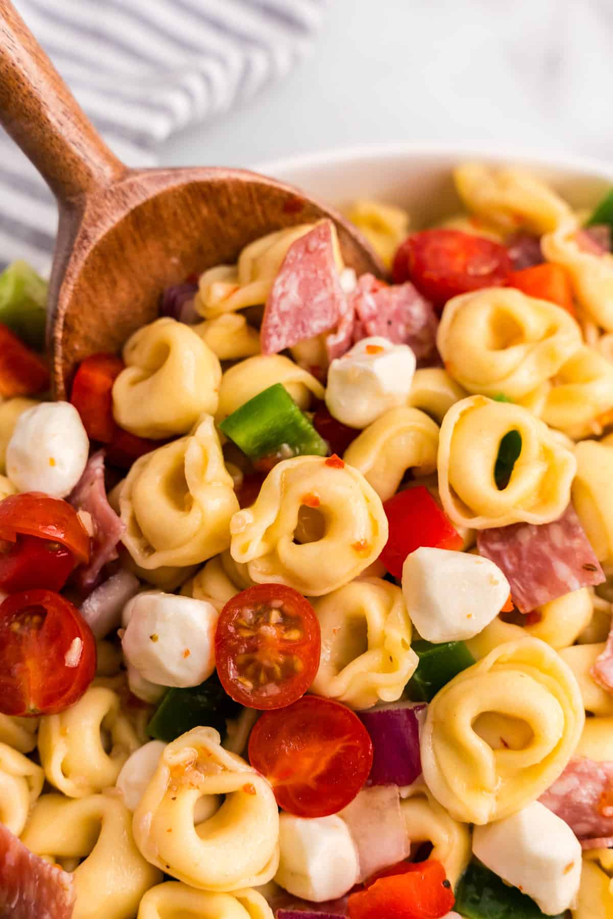 Using wooden spoon to scoop Tortellini Pasta Salad from serving bowl