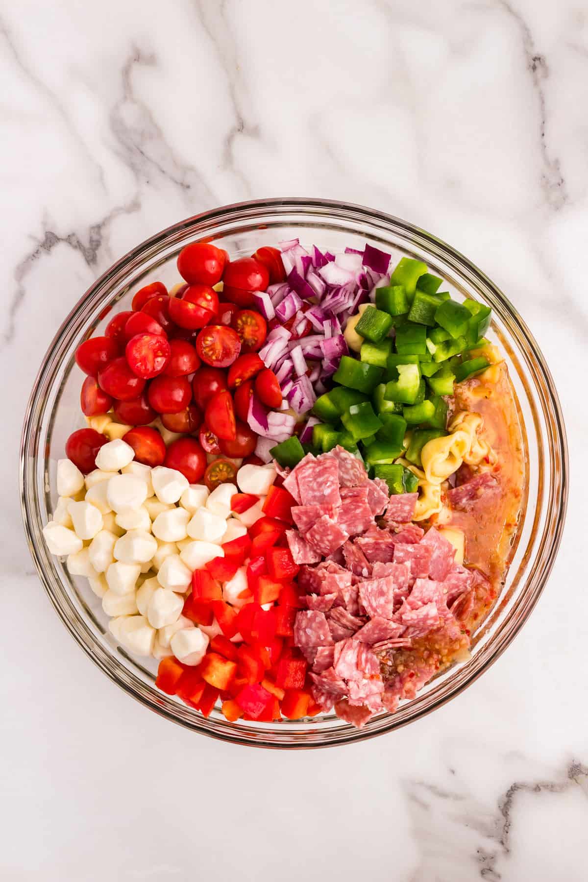 Prepared ingredients added to cooked pasta for Tortellini Pasta Salad recipe in mixing bowl