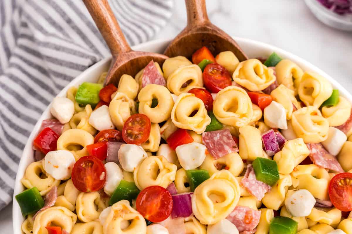 Tortellini Pasta Salad in bowl and using wooden spoon to scoop