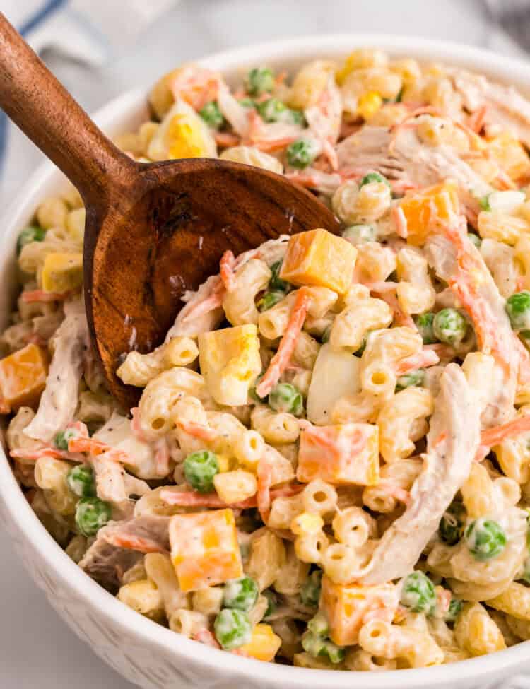 Using a wooden serving spoon to scoop Chicken Macaroni Salad from large bowl
