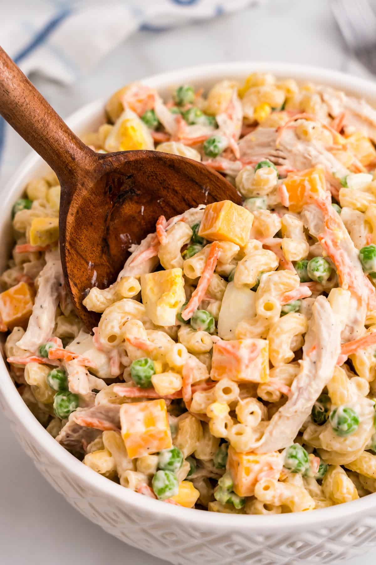Using a wooden serving spoon to scoop Chicken Macaroni Salad from large bowl