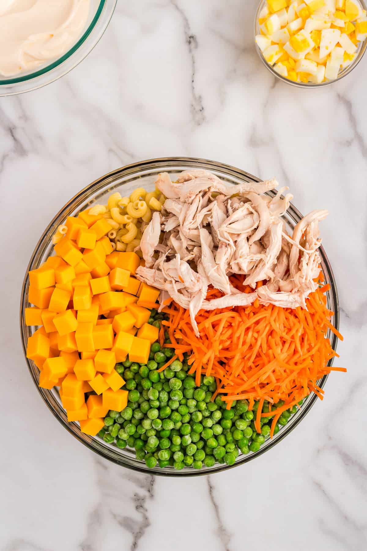 Adding chunked cheese, vegetables, and shredded chicken to noodles for Chicken Macaroni Salad