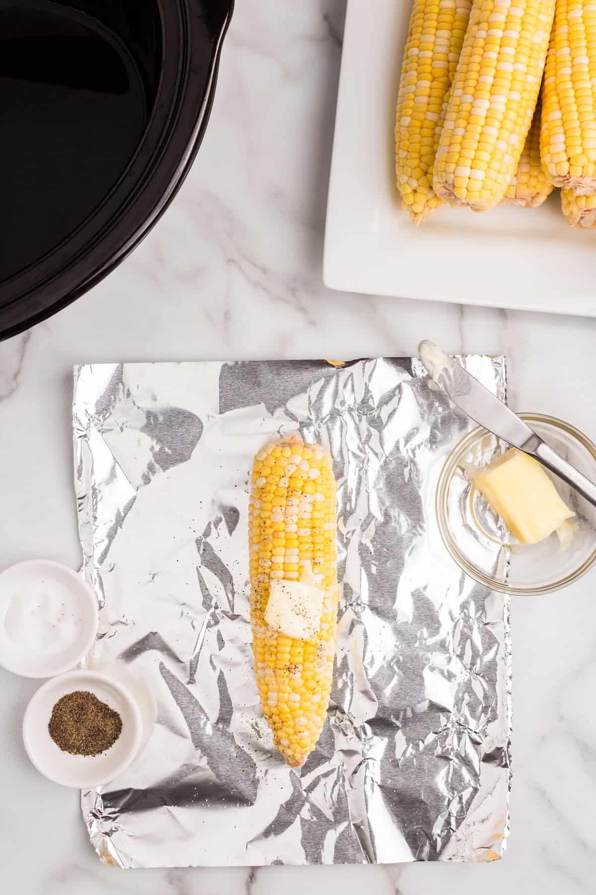 Seasoning corn with salt, pepper, and butter before rolling in tin foil for Crock Pot Corn on the Cob recipe