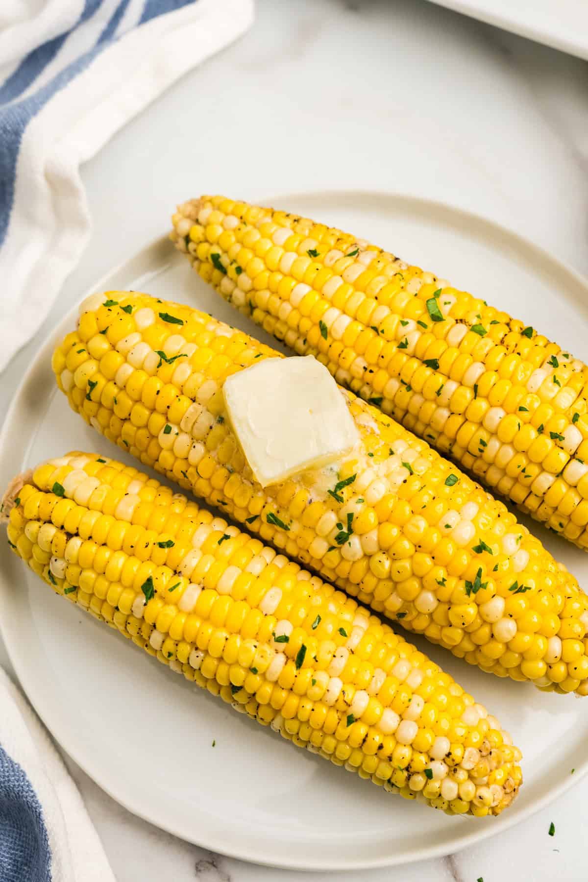 Cooked Crock Pot Corn on the Cob arranged on plate with pads of butter melting overtop