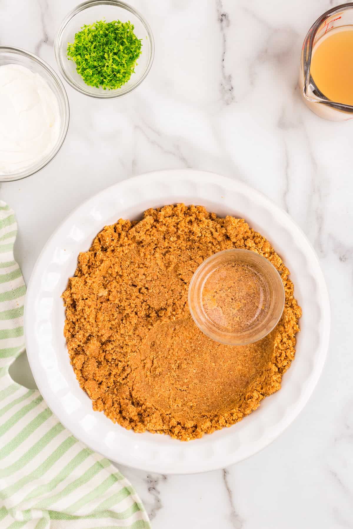 Adding Key Lime Pie crust to pie pan and using glass to press it down into the pan