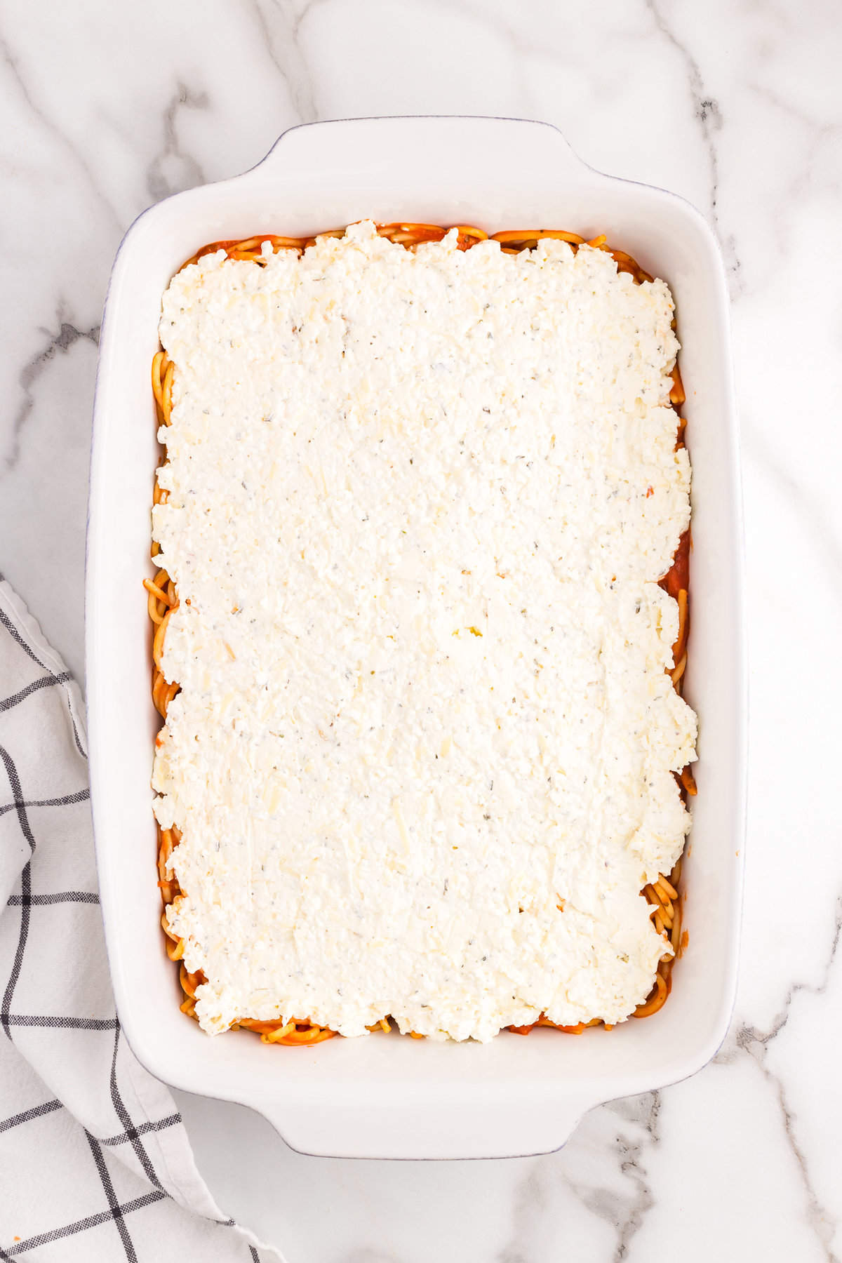 Evenly spreading cheese mixture over sauced noodles for Million Dollar Spaghetti Casserole