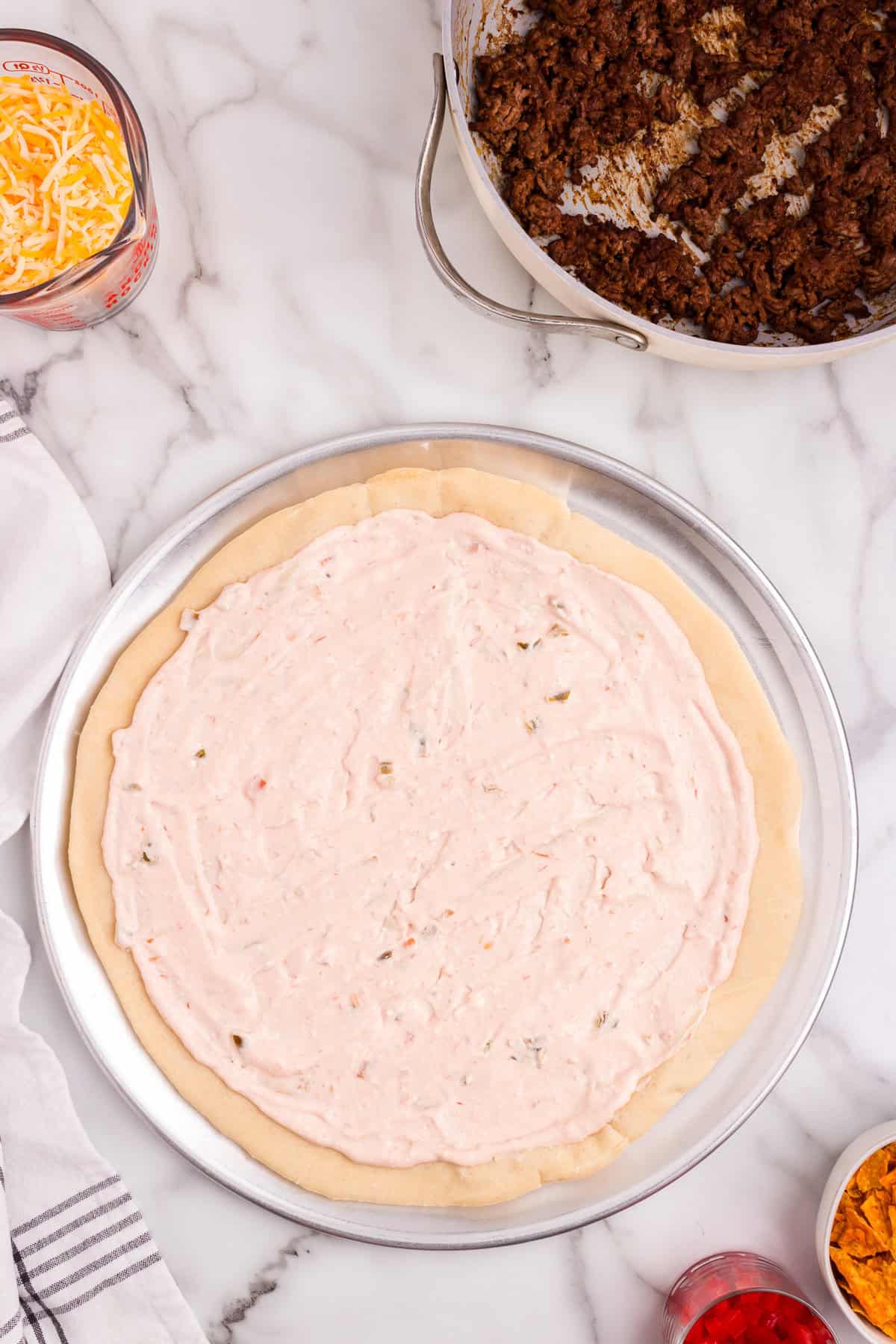 Spreading sour cream, cream cheese, and salsa mixture on pizza dough for Taco Pizza recipe