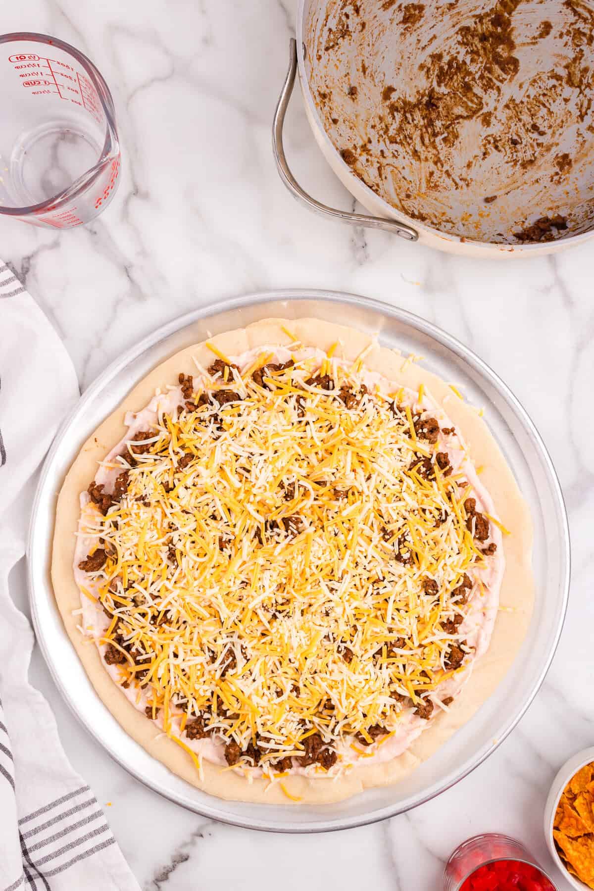 Adding taco meat and shredded cheese to Taco Pizza prior to baking