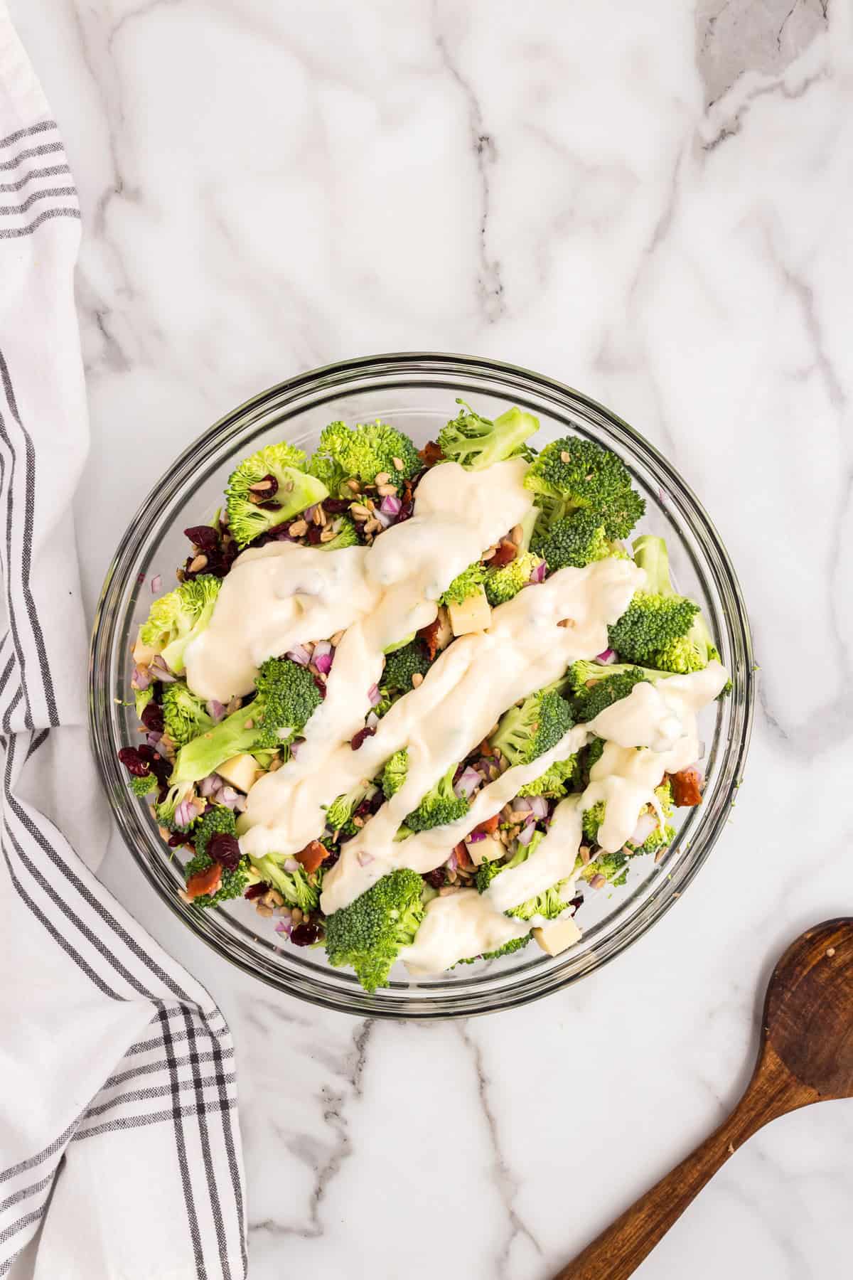 Adding dressing to mixed ingredients for Broccoli Salad recipe in mixing bowl