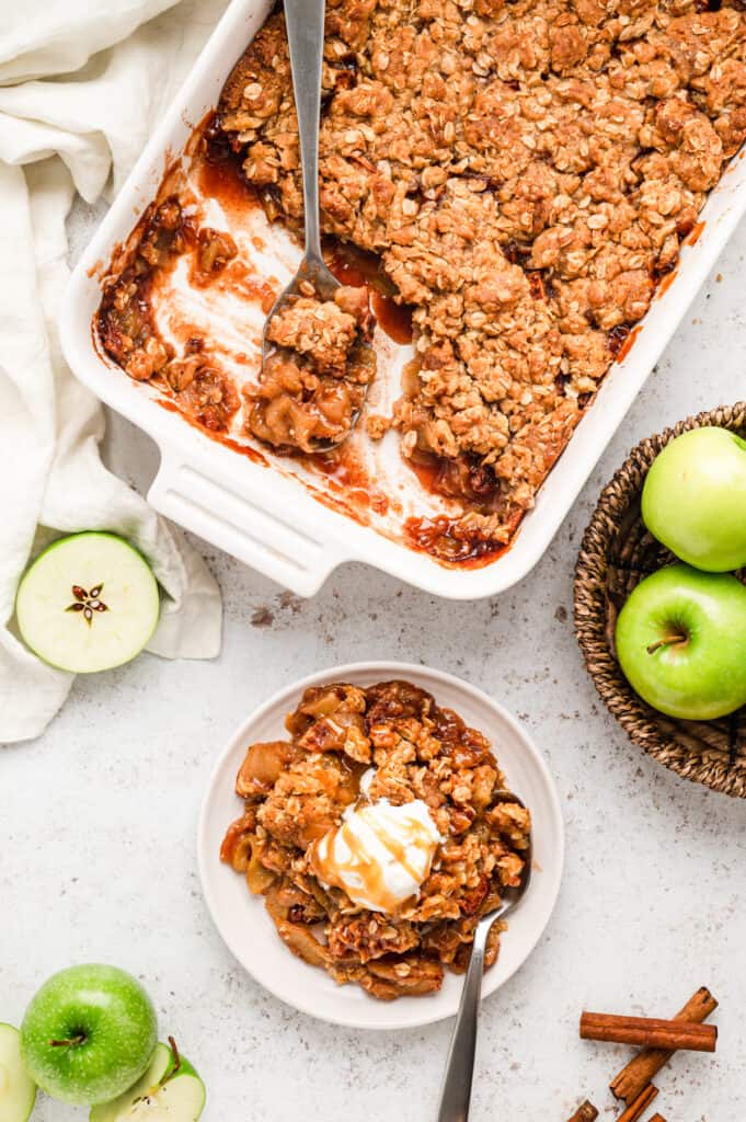 Apple crisp scooped from baking pan and in serving bowl topped with ice cream and caramel