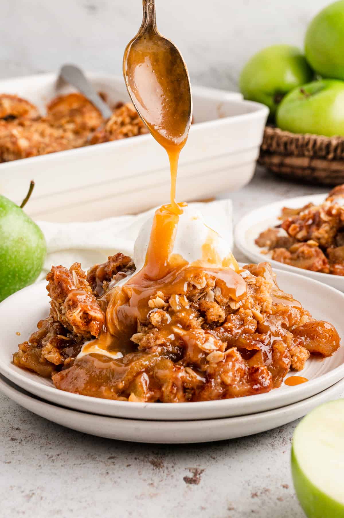 Easy Apple Crisp in bowl with vanilla ice cream and drizzling caramel on top with spoon