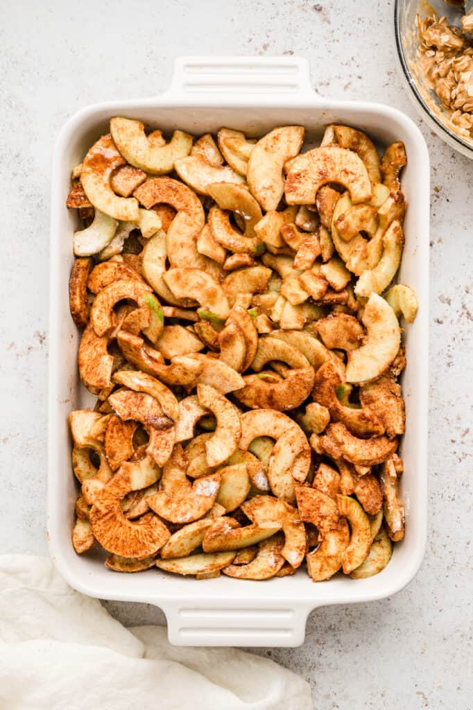 Seasoned apple slices spread out in 9x13 baking pan for Easy Apple Crisp recipe