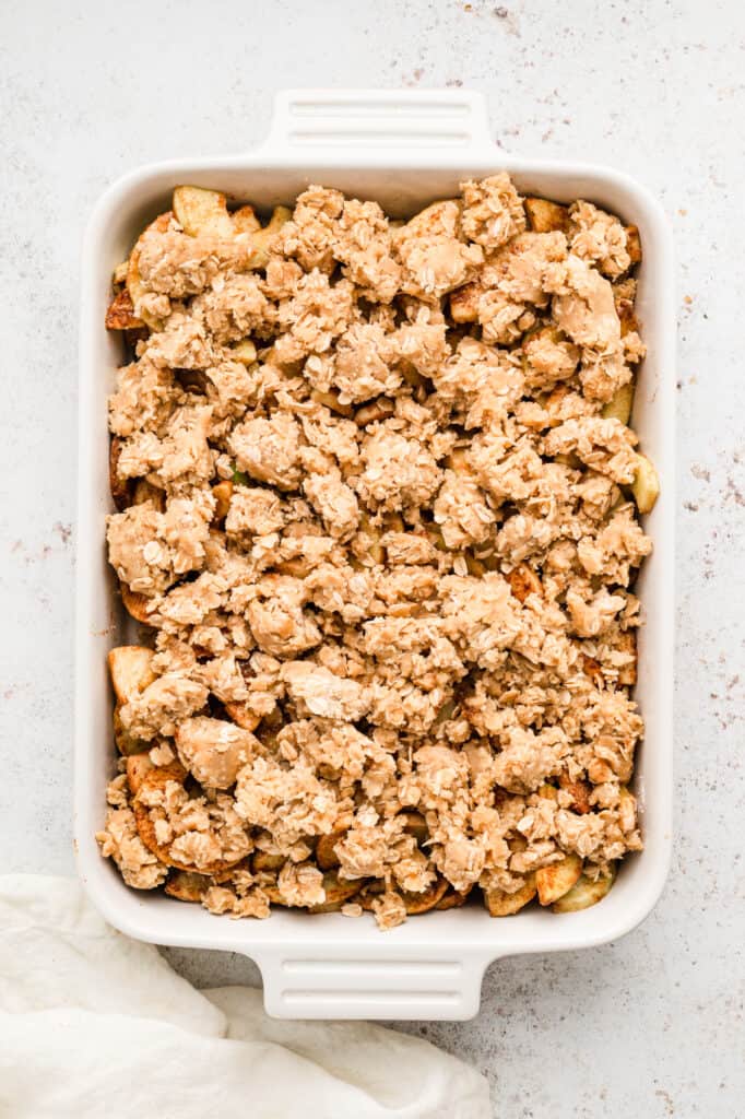 Covering seasoned apples with Apple Crisp topping in baking dish